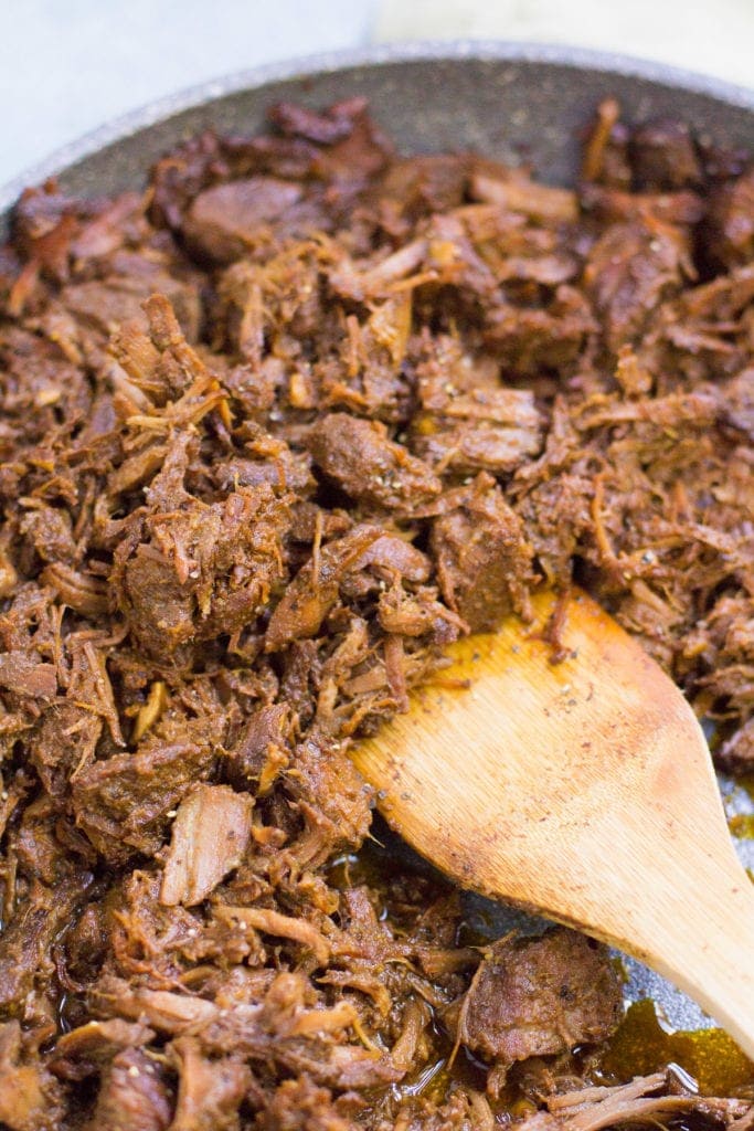 A close up shot of shredded healthy crockpot beef and broccoli with a wooden spoon.