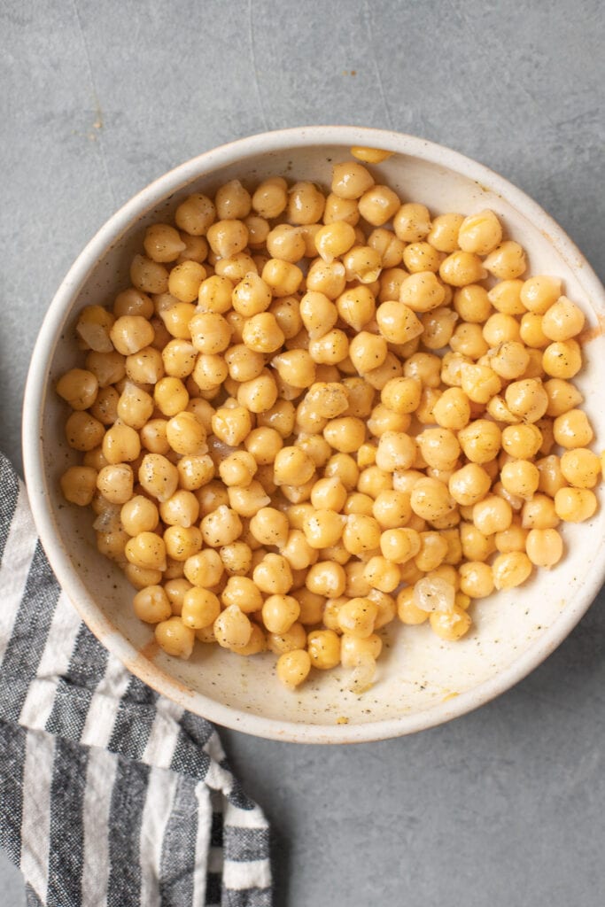 chickpeas in a bowl tossed with olive oil and spices before being baked in the oven