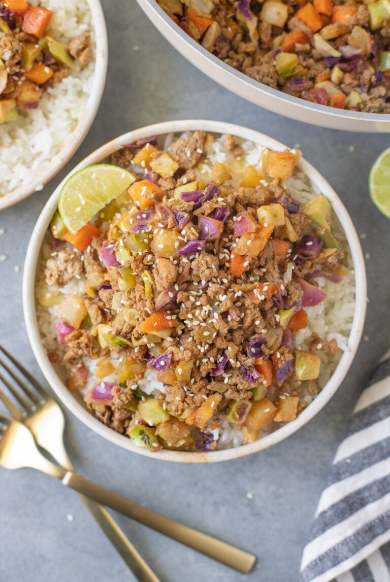 Ground Turkey Skillet in a white bowl with gold forks and a pan on the side on a grey background