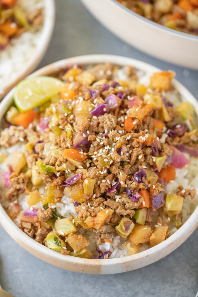 A close up of a white bowl of a ground turkey skillet dinner with white rice on a grey background