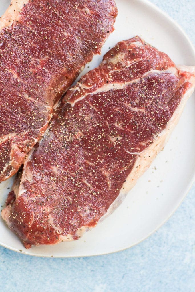 Seasoned steaks getting ready to be placed in a cast iron skillet.