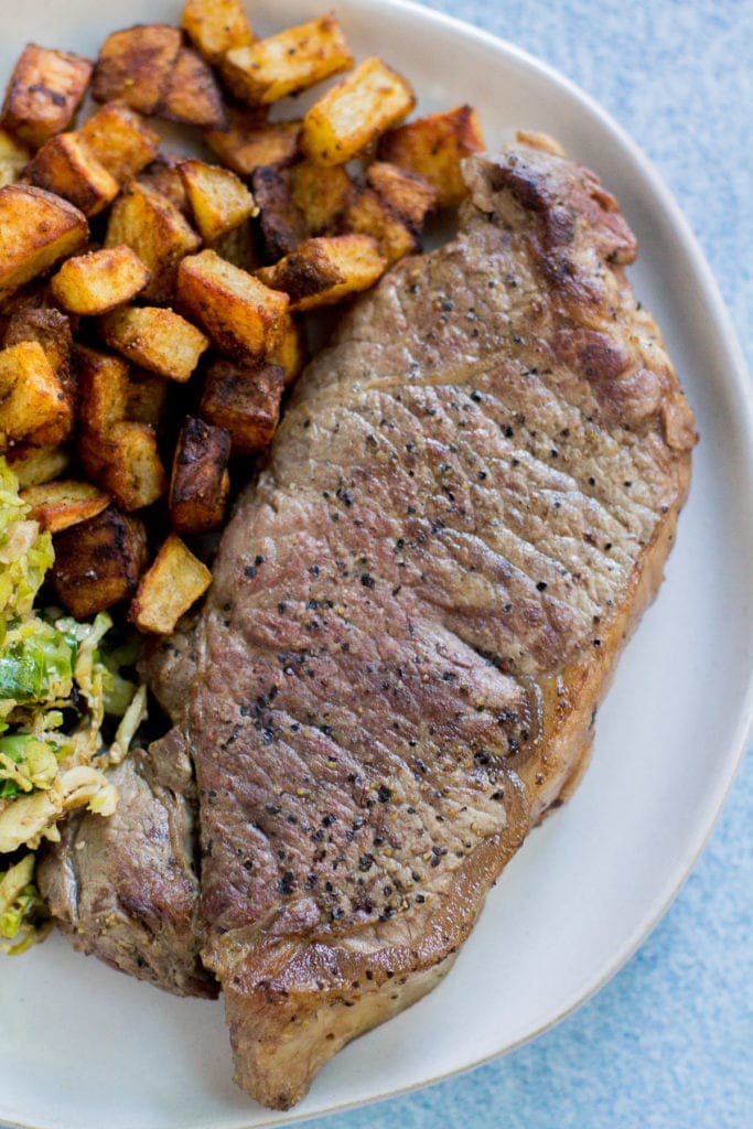Perfectly Cooked cast iron steak on a white plate with potatoes and vegetables