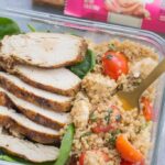 A close up image of Chicken Caprese Quinoa Meal Prep Bowls with a gold fork taking a bite out of it + a granola bar off to the side