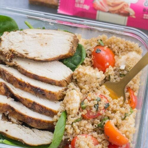 A close up image of Chicken Caprese Quinoa Meal Prep Bowls with a gold fork taking a bite out of it + a granola bar off to the side