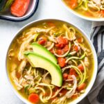 A bowl of Paleo Chicken Soup on a grey background with veggies and a linen off to the side