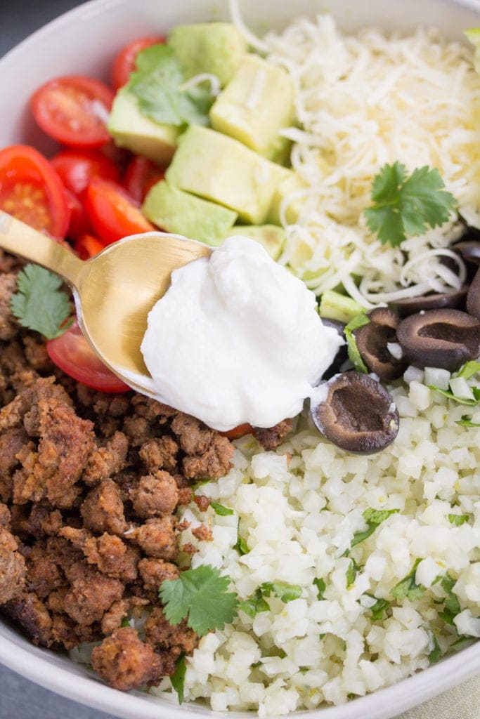 A spoonful of yogurt being added to taco cauliflower rice bowls