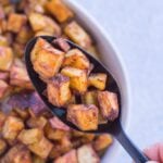 a spoon holding up crispy mexican potatoes from a white bowl