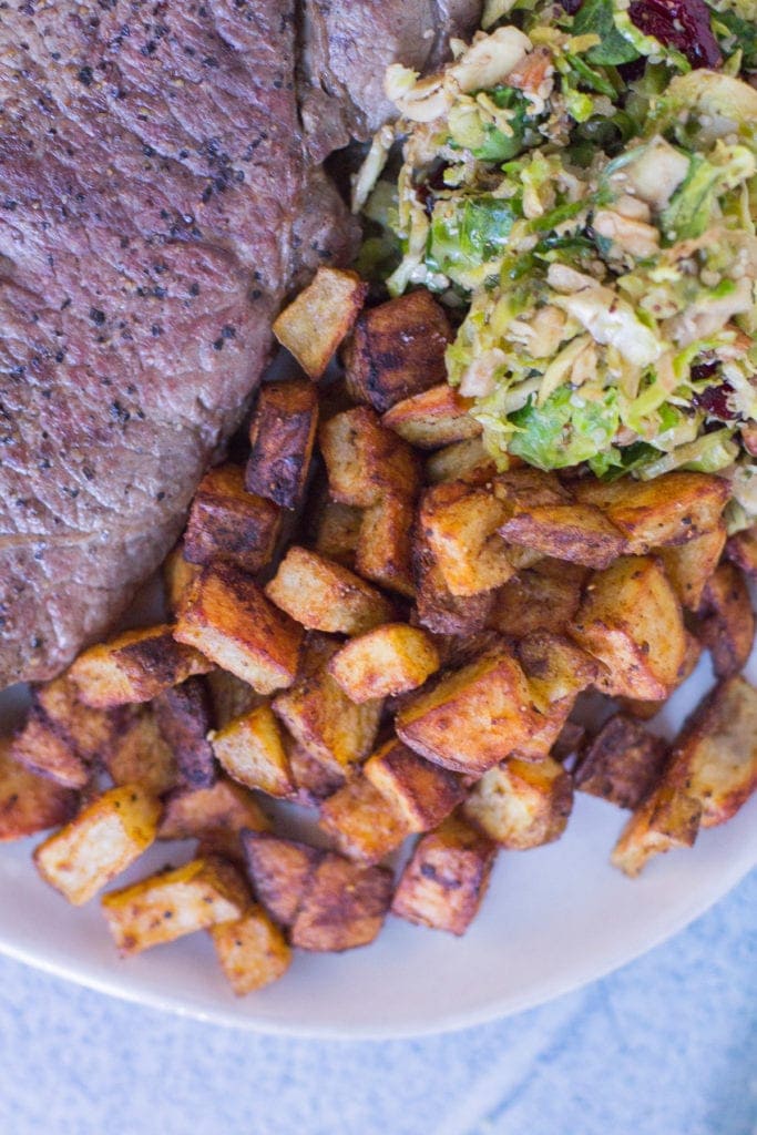 Mexican potatoes on a white plate with steak and brussels sprouts