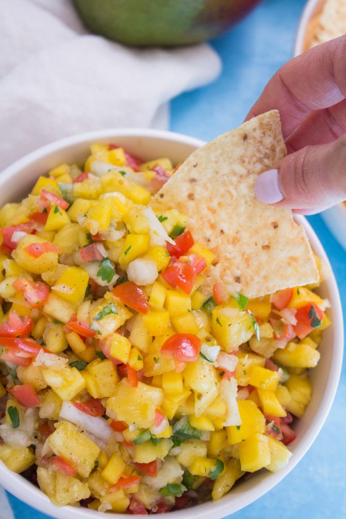 a tortilla chips taking a scoop out of pineapple mango salsa