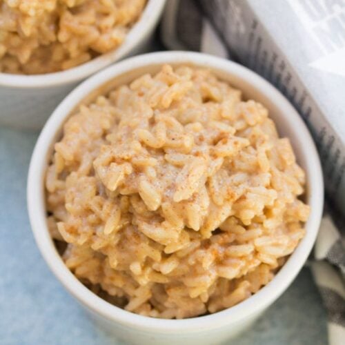A small white bowl filled with delicious creamy vegan rice pudding on a blue background.