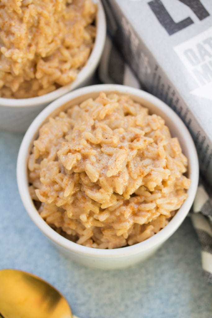 A small white bowl filled with delicious creamy vegan rice pudding on a blue background.