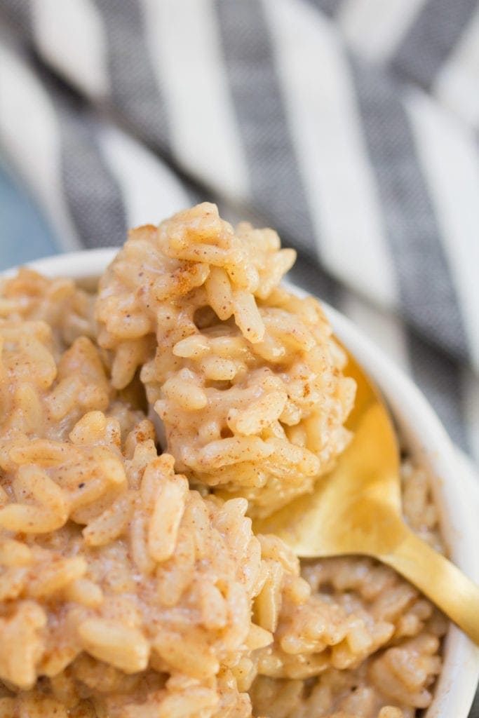 A small bowl of vegan rice pudding with a gold spoon scooping a bite out.