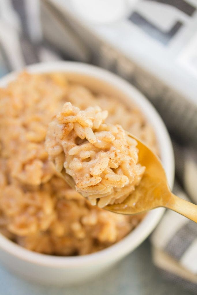 A gold spoon holding up a spoonful of rice pudding from a white bowl