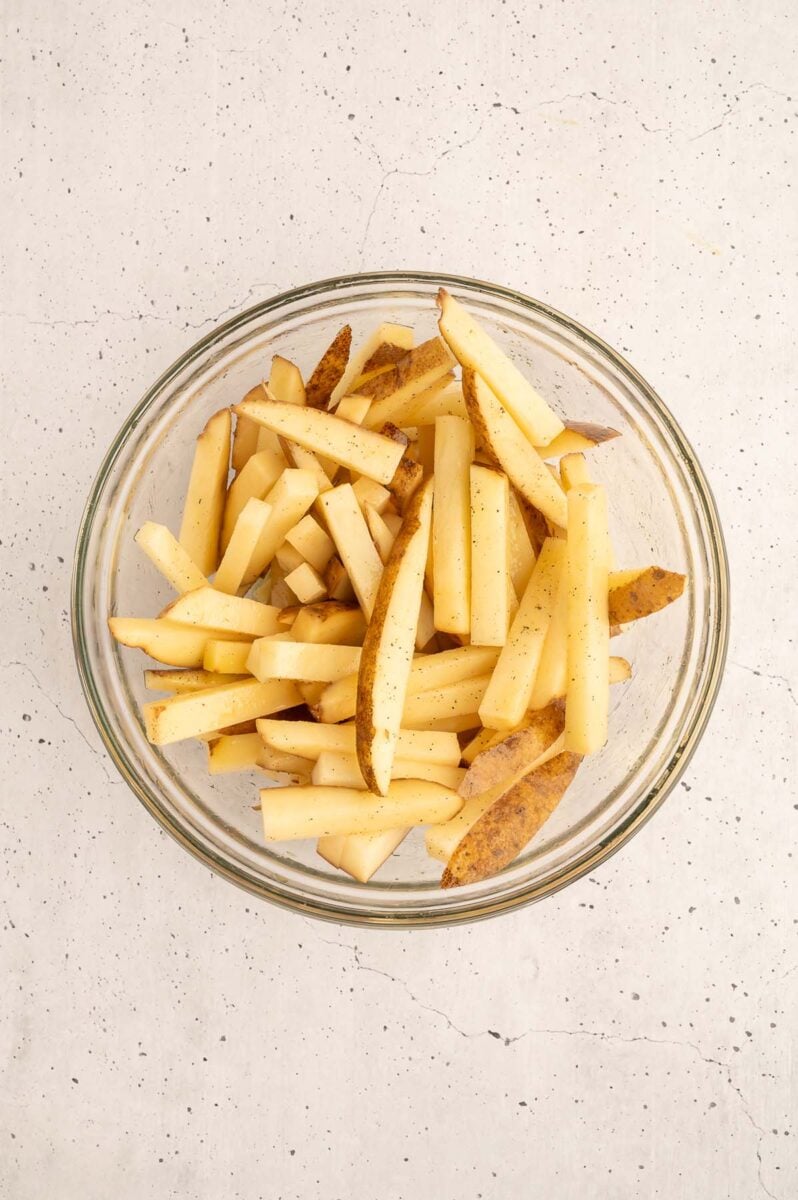 Sliced potatoes in a bowl tossed with olive oil, salt and pepper for healthy baked french fries.