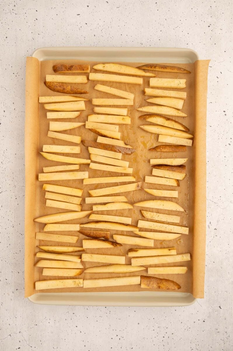 Uncooked french fries on a parchment lined baking sheet.