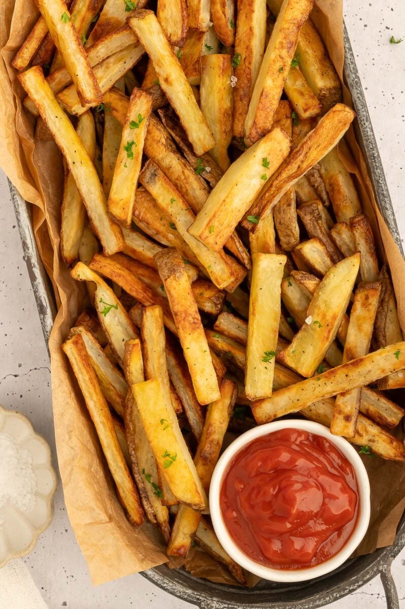 A small bowl of ketchup on the side of baked french fries on a platter.