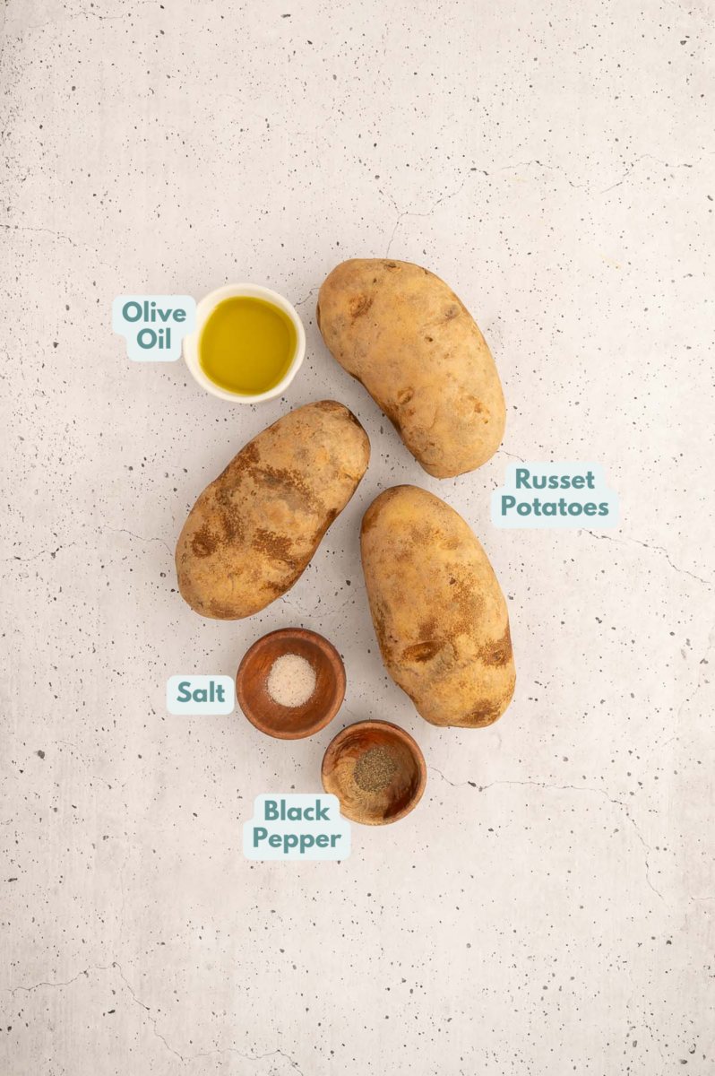 ingredients to make baked french fries on a counter: potatoes, salt, pepper and olive oil