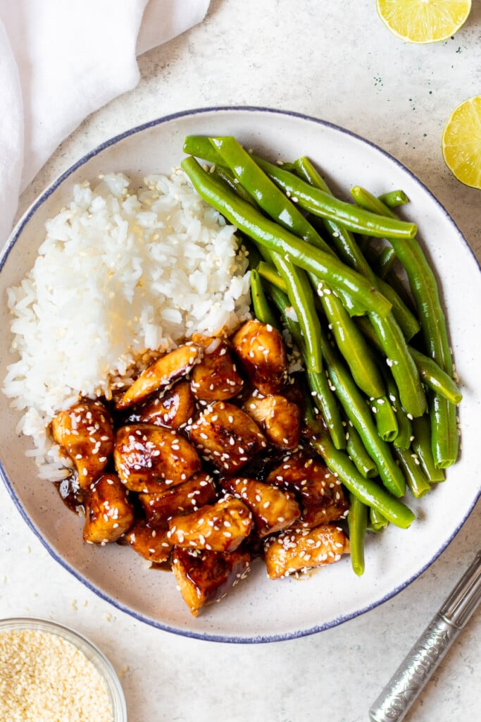 Healthy Sesame Chicken, white rice and green beans on a grey and white plate