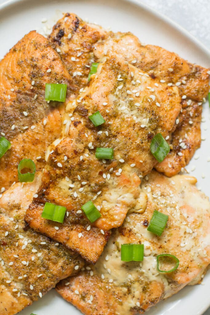 Asian spin Salmon fillets on a white plate with green onion and toasted sesame seeds on top 