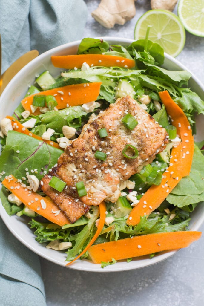 Asian Fresh Salmon over a salad on a grey background. Ginger and limes cut in the top right