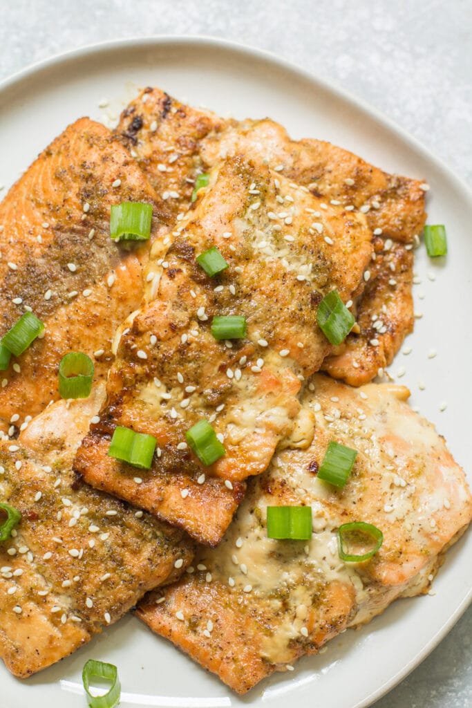 A close up of asian baked salmon on a white plate with green onions on top  - paleo, whole30 and healthy!