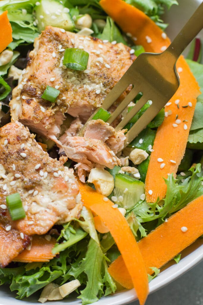 a golden fork taking a bite out of asian baked salmon on a salad