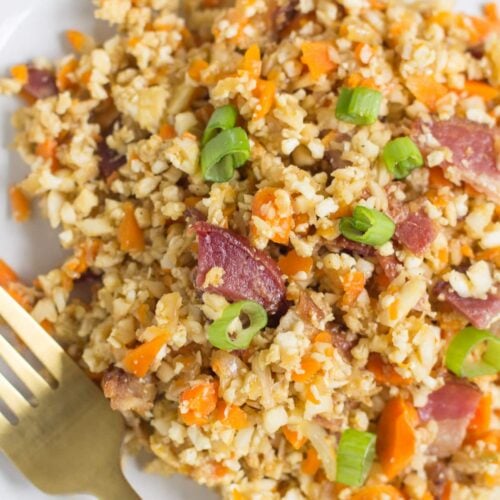 A close up of Breakfast Cauliflower Fried Rice on a white plate with a gold fork.
