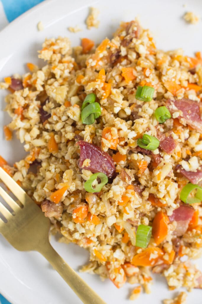 A close up of Breakfast Cauliflower Fried Rice on a white plate with a gold fork.