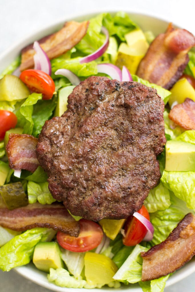 A burger salad with dill pickle vinaigrette in a white bowl