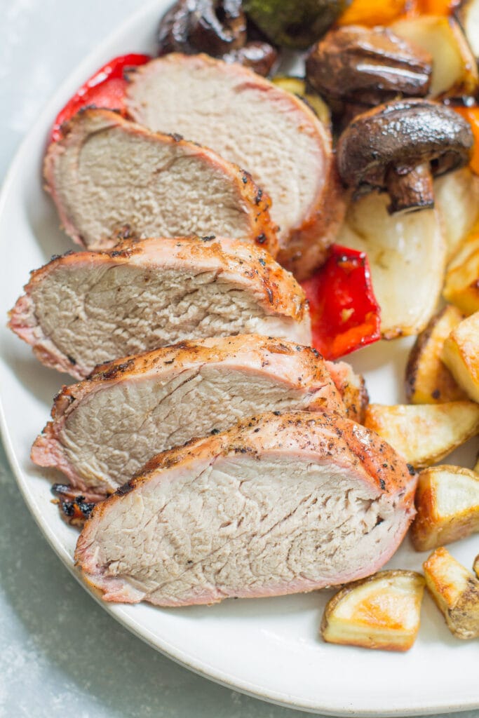 Citrus grilled pork tenderloin on a white plate with vegetables + potatoes all around it.