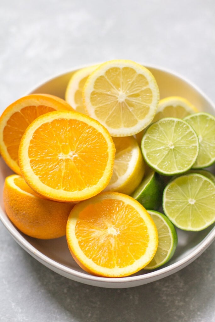 a white bowl filled with citrus fruits.