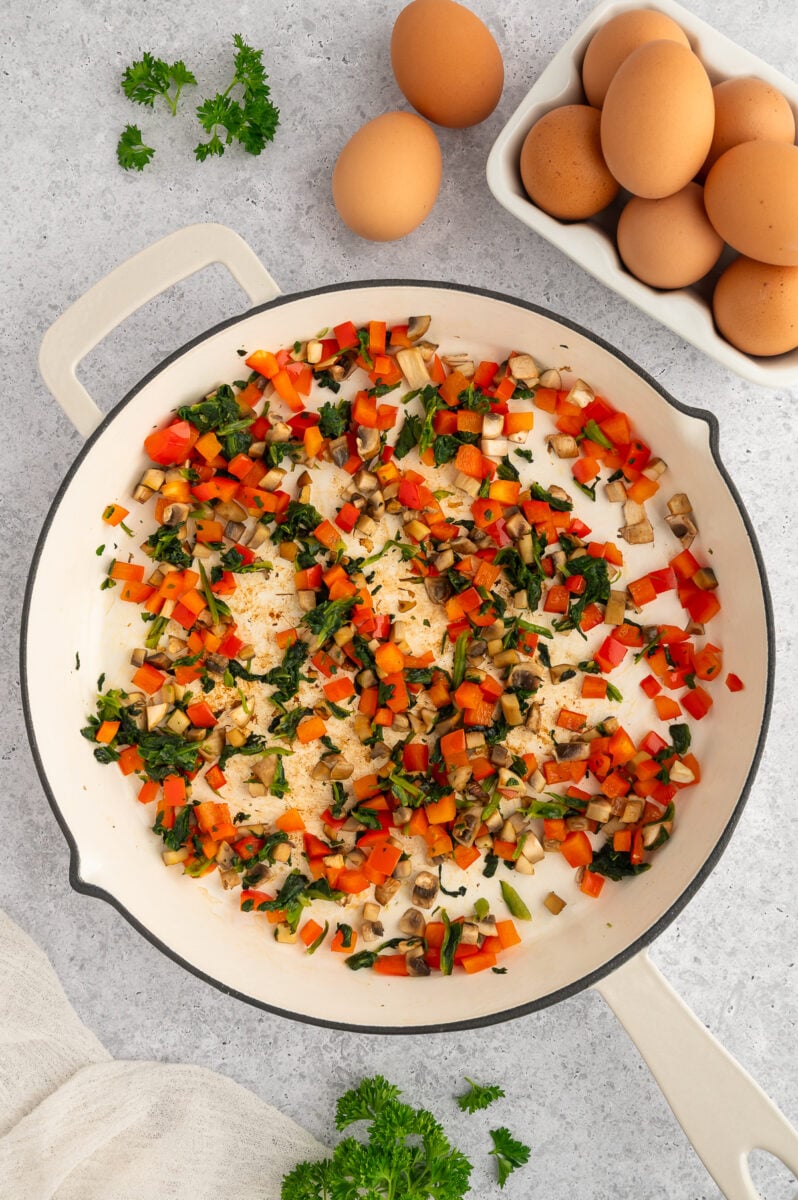 Sautéed chopped veggies in a saute pan with eggs on the side.