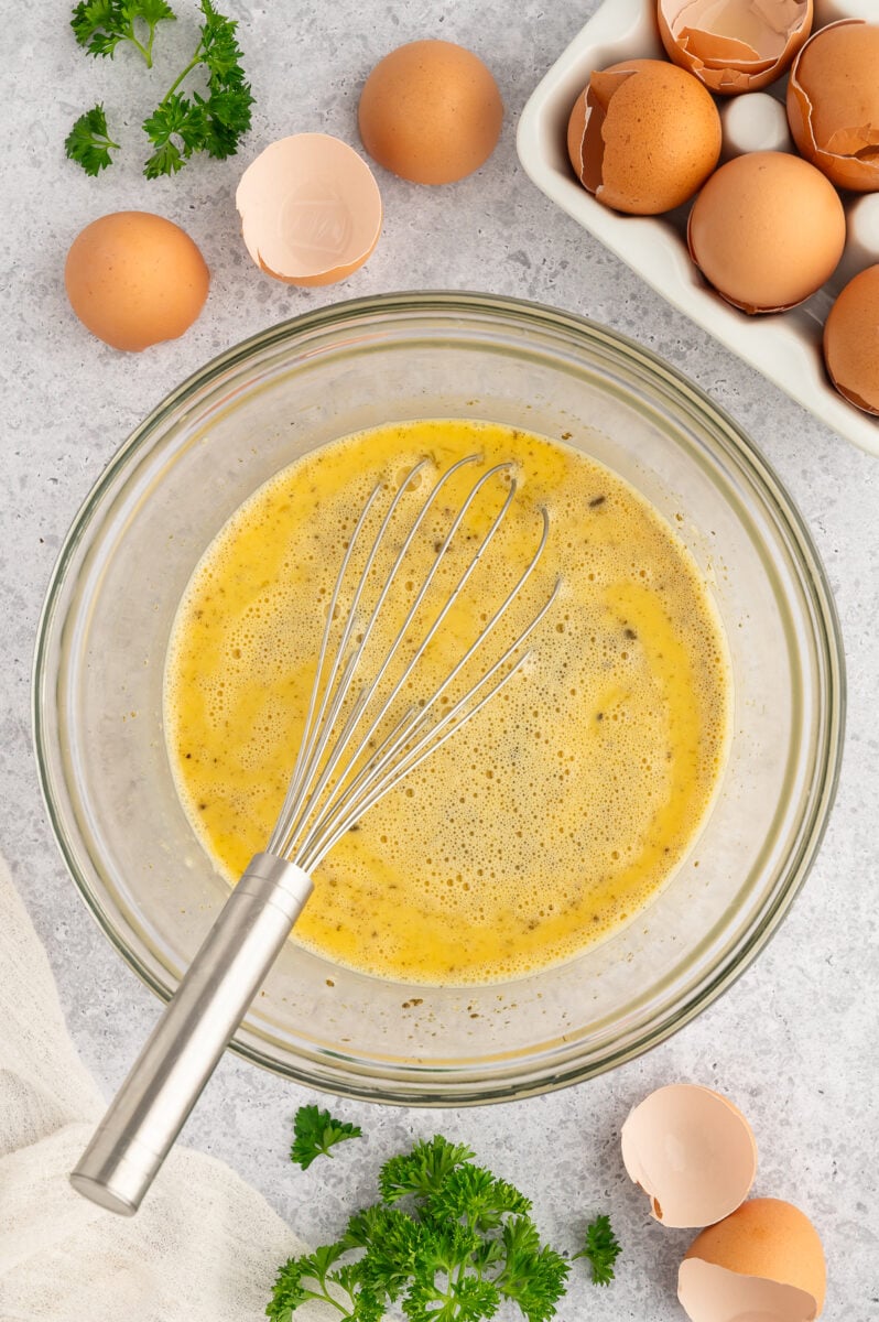 Beaten eggs in a clear bowl with spices and a whisk in it.