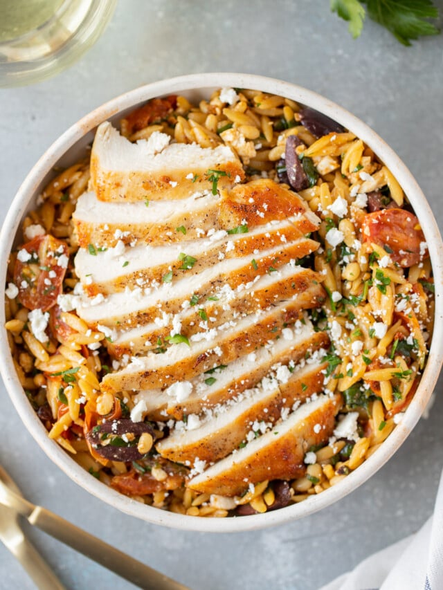 Mediterranean Chicken Orzo on a white dish on a grey background with forks on the side