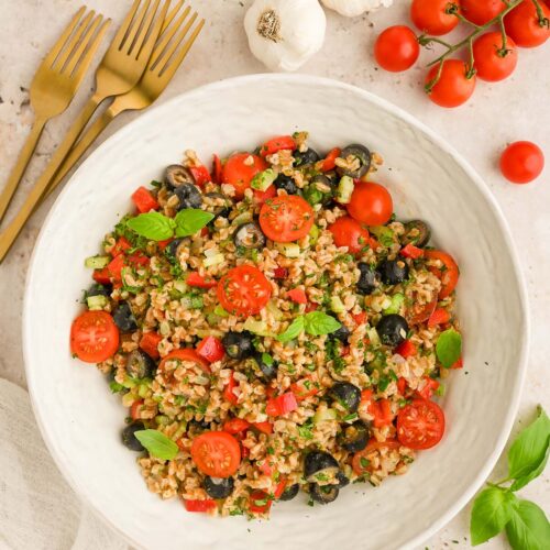 Easy Farro Salad in a white bowl with tomatoes and fresh herbs on the side.
