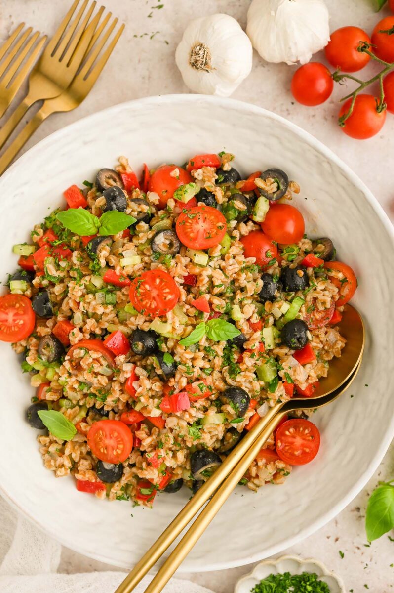 A big white bowl of easy farro salad with gold spoons in it. 