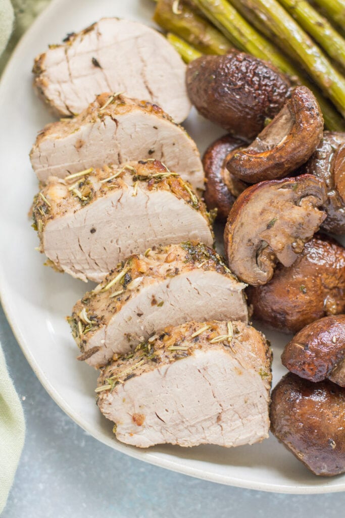 Italian Pork Tenderloin sheet pan dinner on a white plate. pork, mushrooms and asparagus.