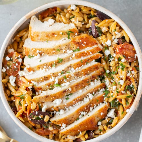 Mediterranean Chicken Orzo on a white dish on a grey background with forks on the side