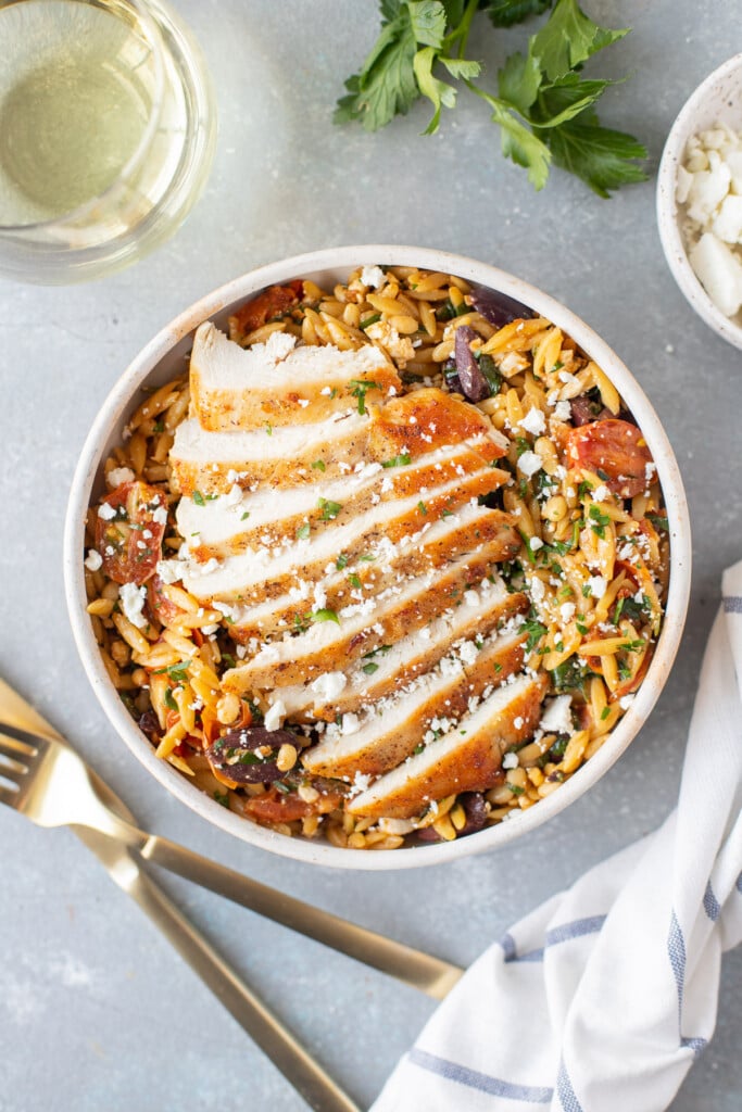 An overhead shot of a white dish of Mediterranean Chicken Orzo on a grey background with forks on the side