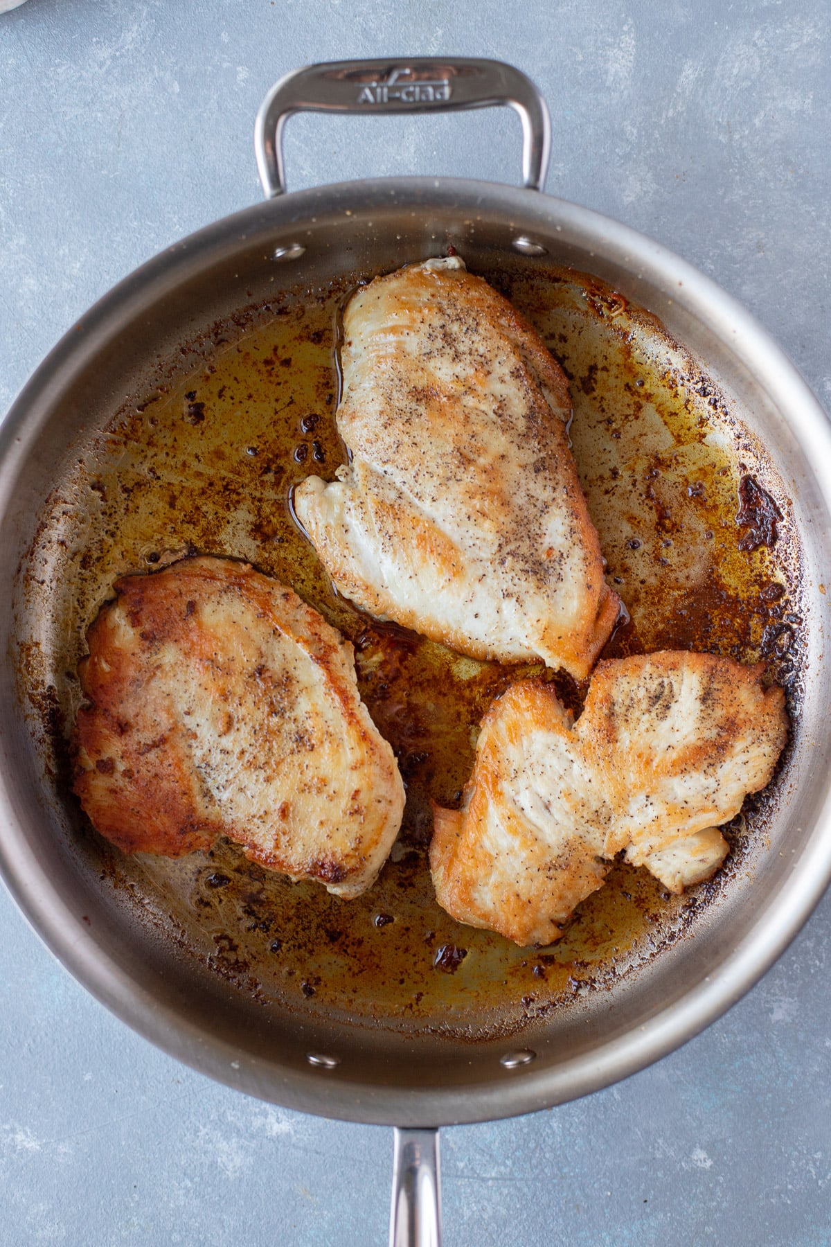 Chicken breasts browning in a pan for mediterranean chicken recipe on a grey background 