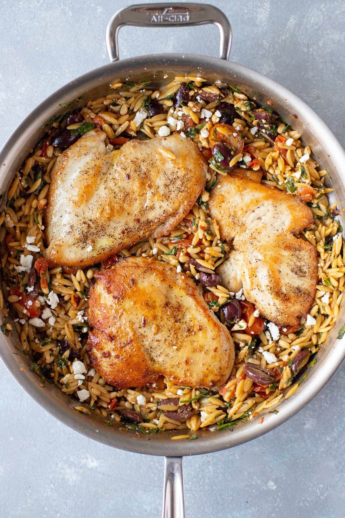 Mediterranean chicken orzo in a pan on a grey background
