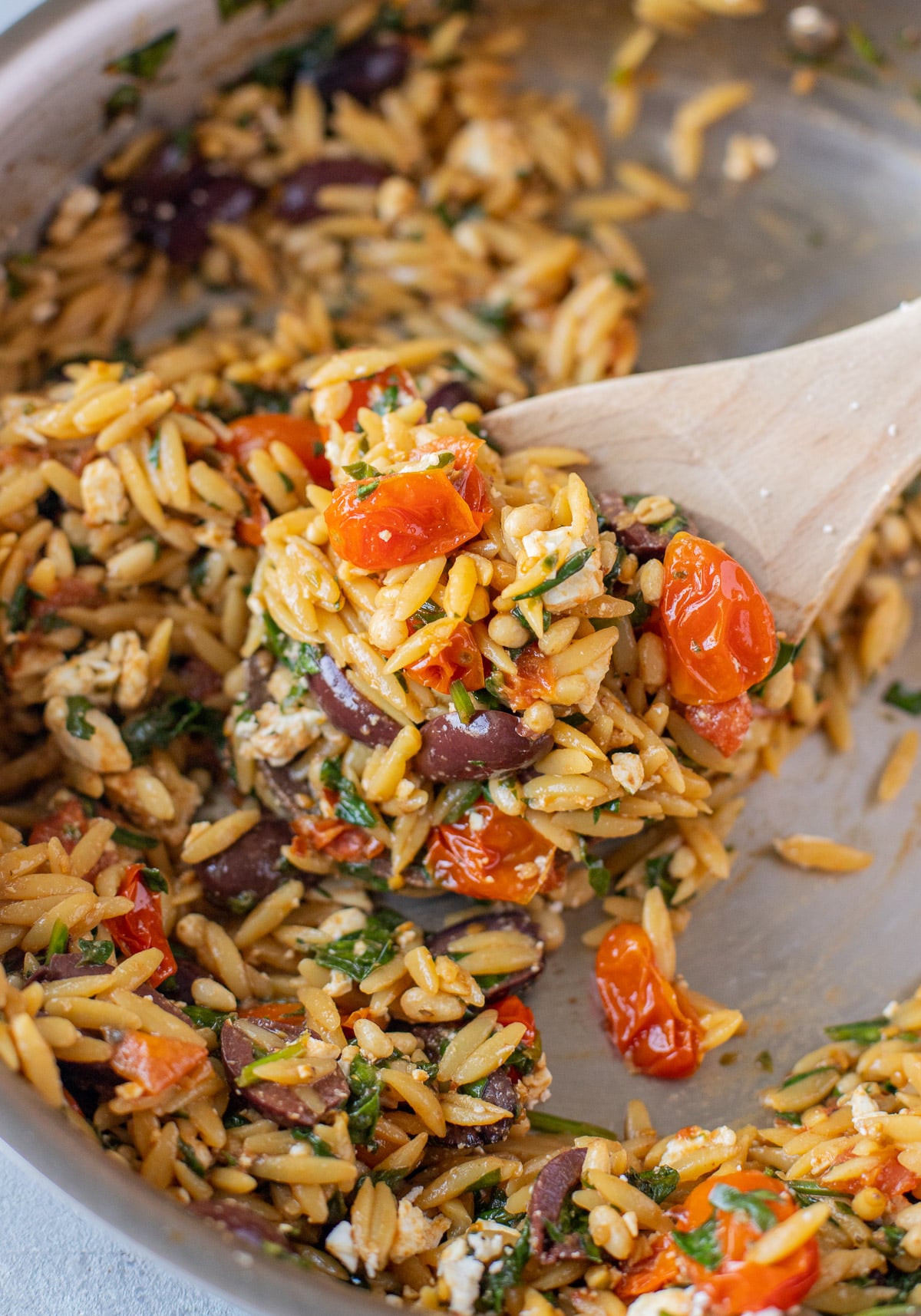 A wooden spoon scooping mediterranean orzo in a pan