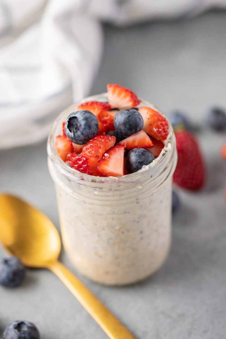 berry overnight oats in a mason jar with a gold spoon on the side on a grey background