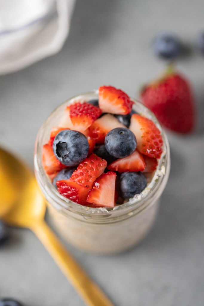 An overhead shot of berry overnight oats in a mason jar on a grey background