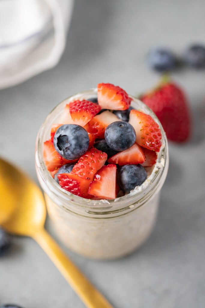An overhead shot of berry overnight oats in a mason jar with berries in the backgroundon a grey background