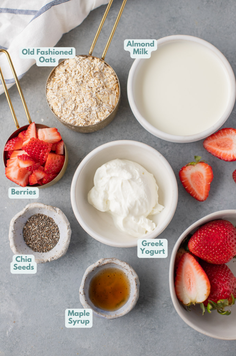 Ingredients for Berry Overnight Oats laid out in small white bowls. Greek yogurt, berries, old fashioned oats, spices, and almond milk.