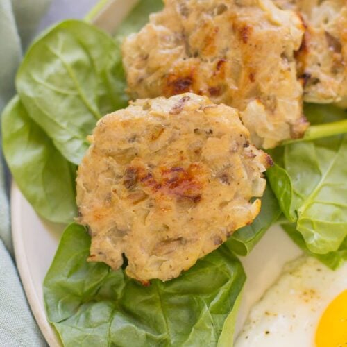 A close up of chicken breakfast sausage on a bed of spinach with eggs on a white plate