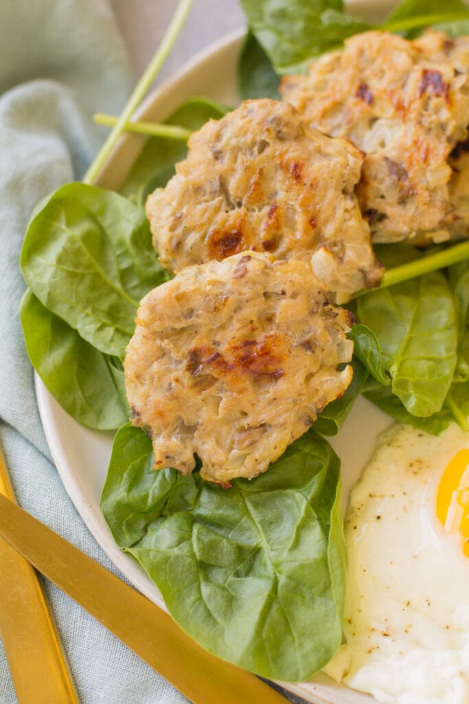 A close up of chicken breakfast sausage on a bed of spinach with eggs on the side.