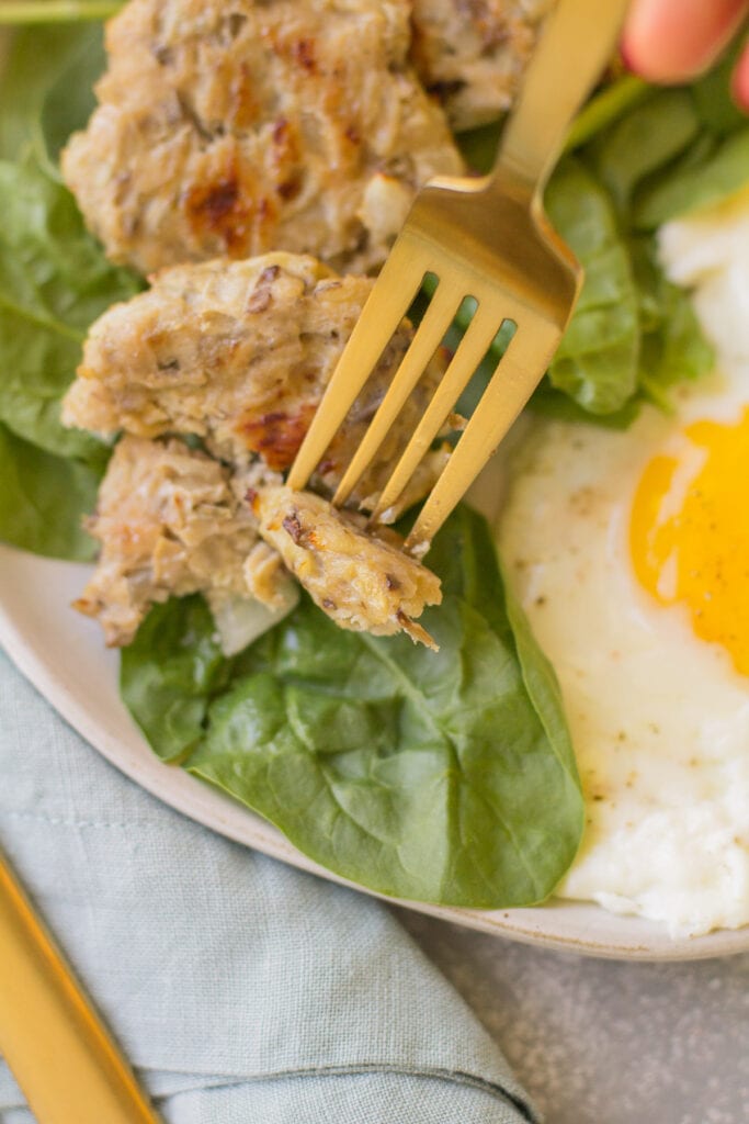 A fork taking a bite out of chicken breakfast sausage on a bed of spinach