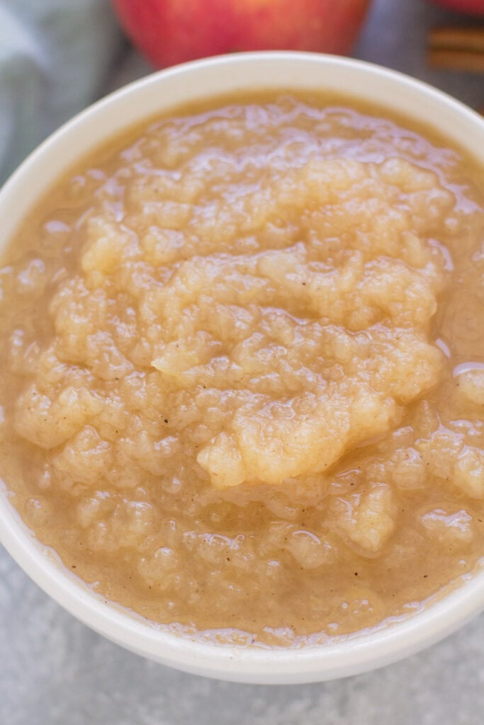 A close up of pressure cooker applesauce in a white bowl with apples behind it.